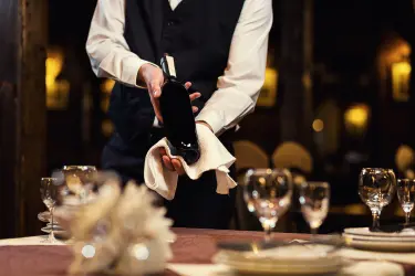 Butler presenting a wine bottle at a formal dining table, representing a professional butler recruitment guide.