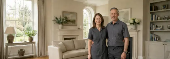 Domestic couple in uniform standing in an elegant private home, representing hands-on household support.