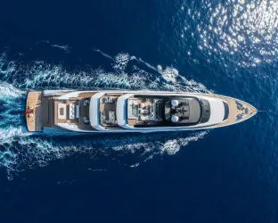 Aerial view of a luxury superyacht cruising across deep blue sea with elegant decks and white ocean wake.