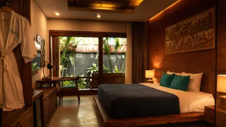 Warmly lit luxury hotel bedroom with wooden interiors, a neatly made bed, hanging robe, and garden view through large glass doors.