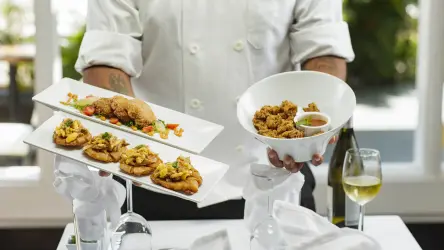 Private chef presenting plated canapés and a bowl of appetisers with wine.