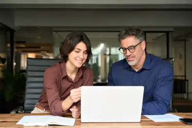 Family office director reviewing documents with a client on a laptop in a private office setting.