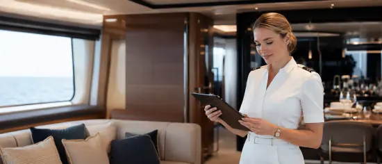 Chief stewardess reviewing a tablet in a luxury yacht lounge with sea views.